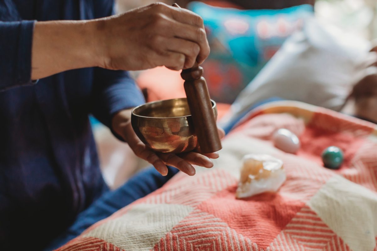 Van playing a singing bowl beside crystals on a colourful blanket