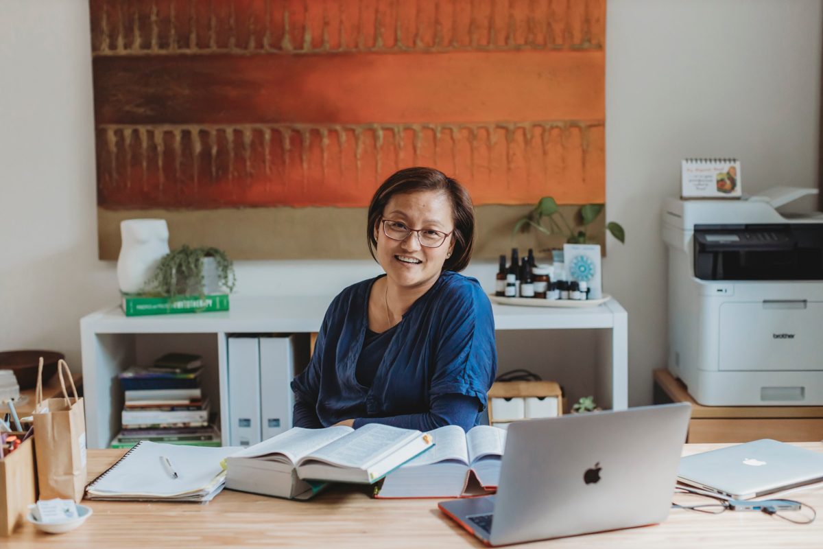Van Seng smiling at her desk with open reference books and a laptop