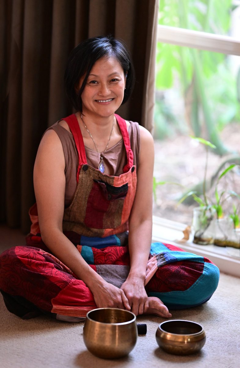 Van Seng smiling, sitting cross legged on the floor beside two singing bowls