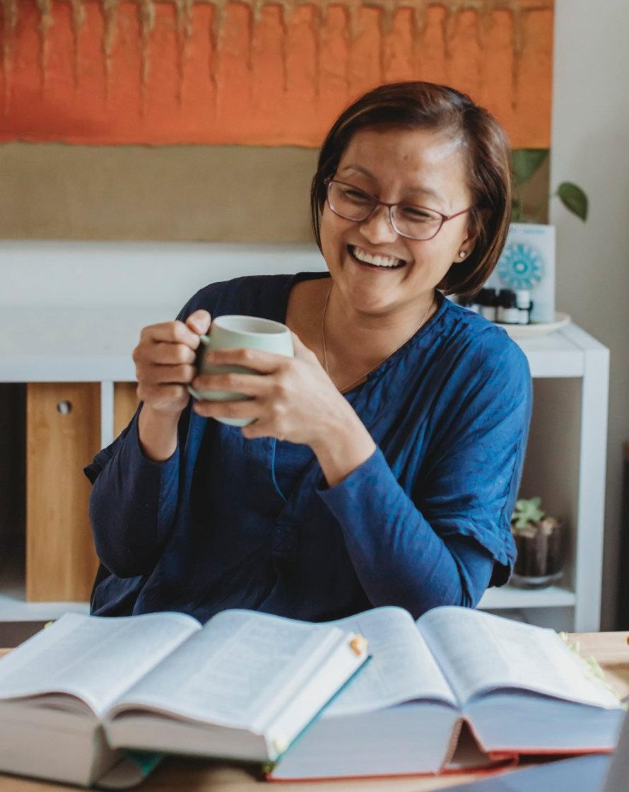Van Seng laughing with a cup of tea at her desk, with open reference books in front of her
